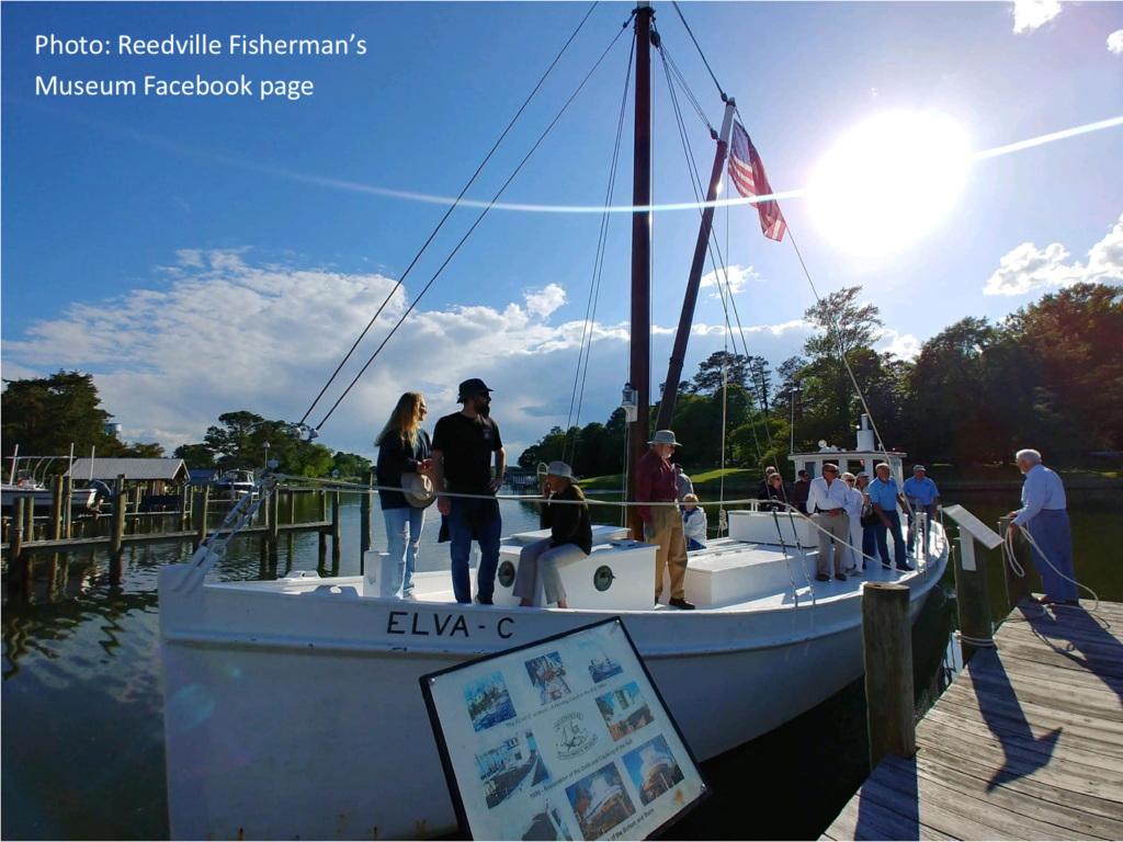 about a dozen people explore an historic sailing vessel, the Elva-C, moored at a dock