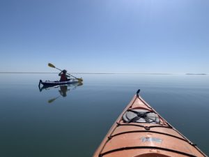 bow of an orange kayak with another kayaker up ahead, kayaking to Virginia's barrier islands