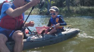 kid holds a net with a fish in it while sitting in kayak