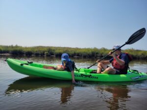 adult and kid go kayaking in a tandem green kayak through a marsh