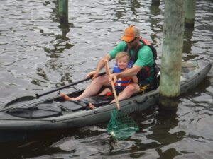 man and kid sit in a kayak while catching a crab in a net