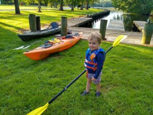 small kid holds a kayaking paddle next to a boat ramp